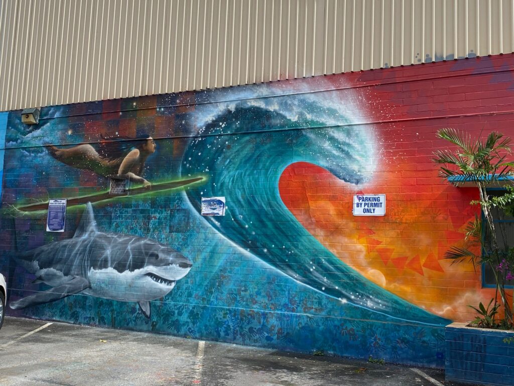 Colorful mural in Kaka'ako with a wave, female surfer and a shark under the water. 