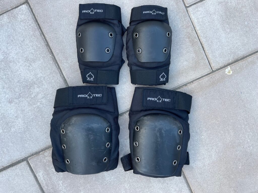 An image of Pro-Tec black knee and elbow pads on the ground facing up. 