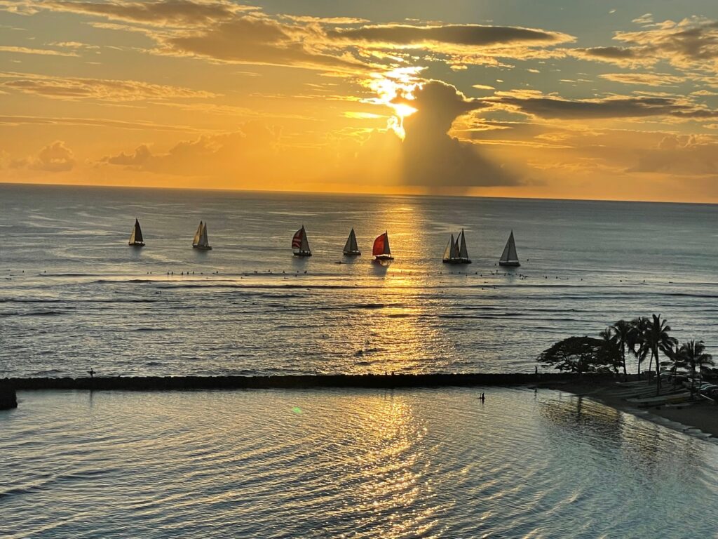 Several sailboats at sunset in Waikiki, Hawaii with setting sun in the background. 
