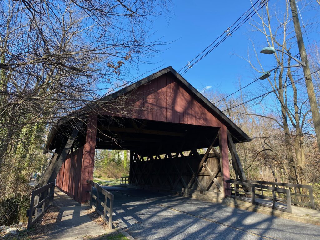The Scarborough Covered Bridge in Cherry Hill, NJ. This brown, wooden bridge is pictured with blue skies behind it. 