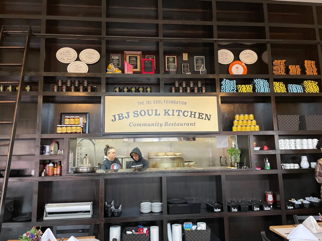The interior sign at JBJ Soul Kitchen with the kitchen beyond it. Sign says "The JBJ Soul Foundation community restaurant"